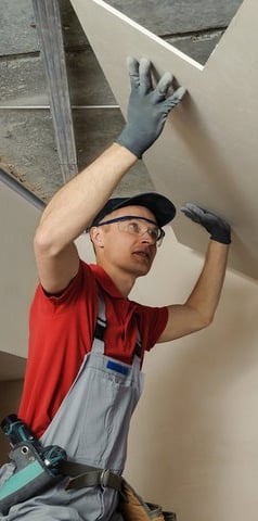 worker adding fresh drywall to a ceiling repair