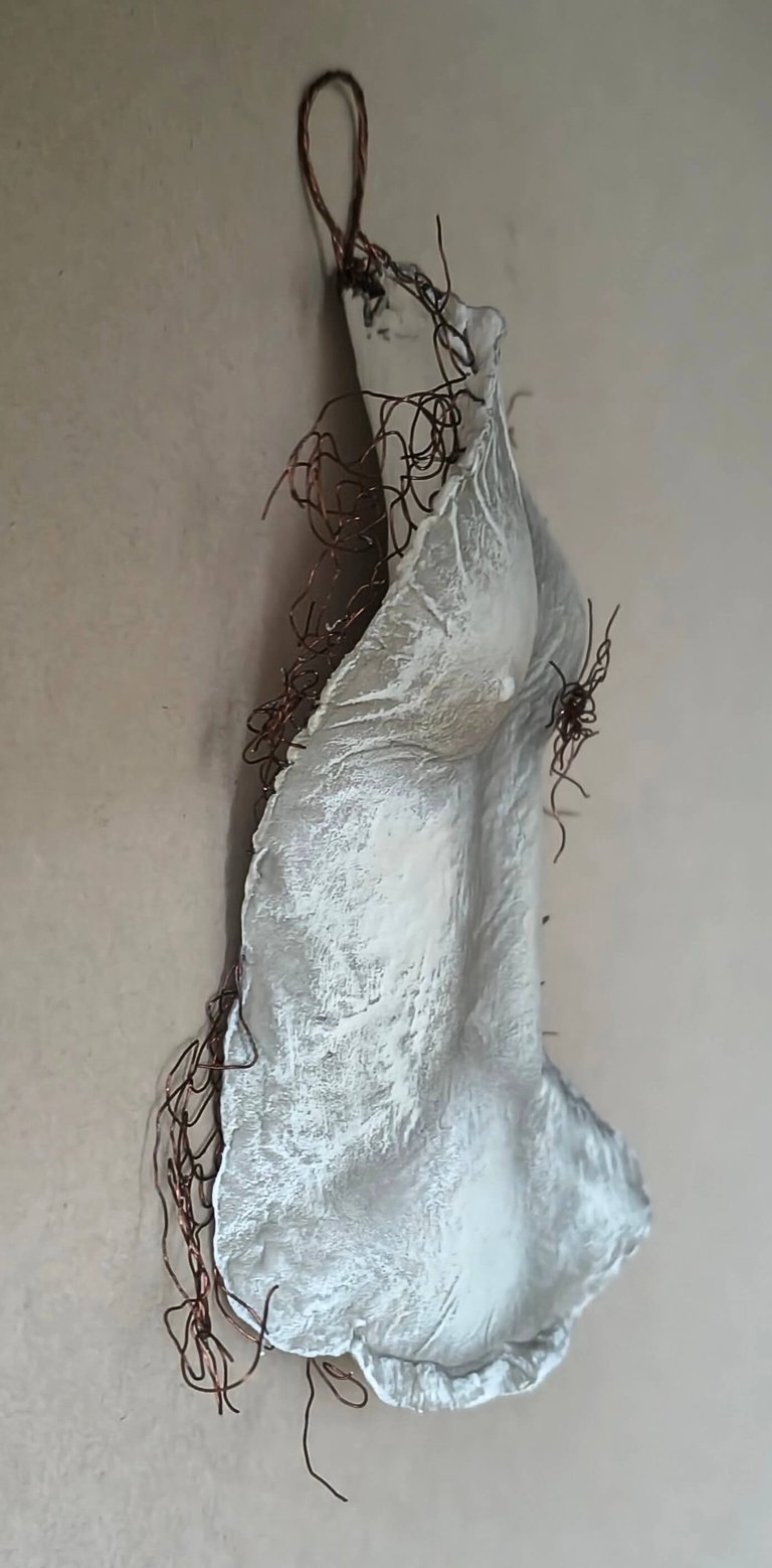 A hanging relief sculpture of a female torso with wire around it and protruding through it.