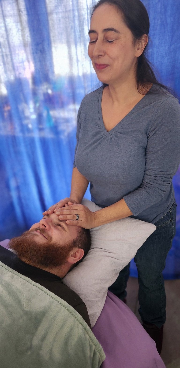 Professional practitioner performing a relaxing Reiki energy healing session on a man's forehead.