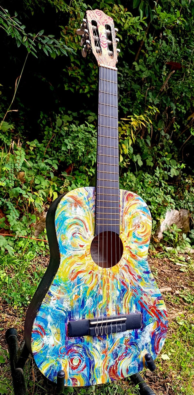 peinture sur guitare aux couleurs vives, avec un soleil autour de la rosace et des formes abstraites