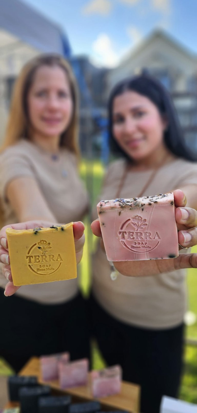 two women holding soap bars in front of a table