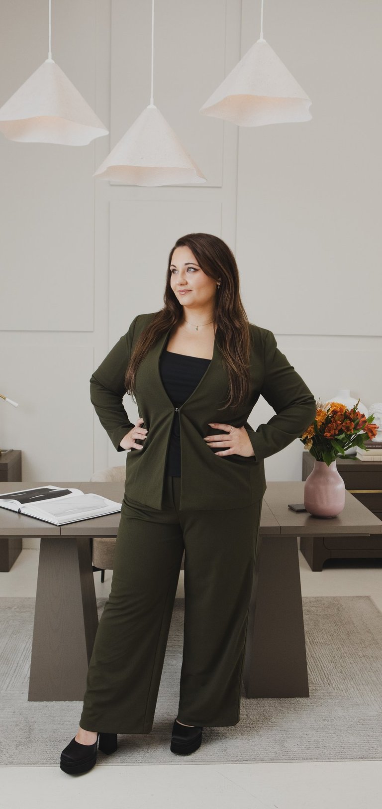 Professional businesswoman in olive green suit posing in modern office studio.