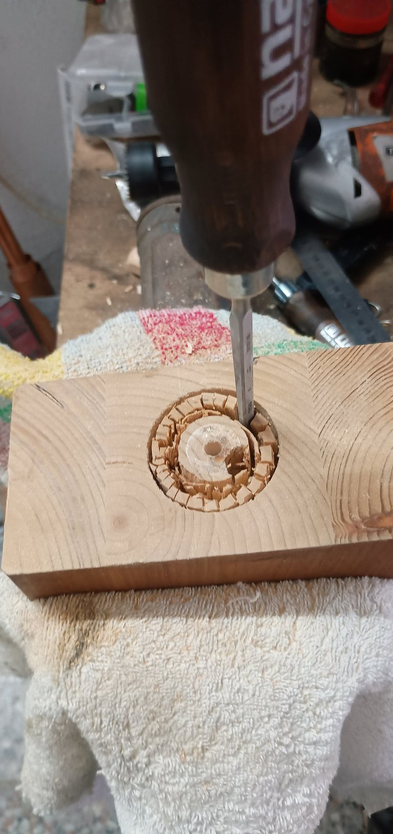 Hand chisel carving a circular recessed hole into a wooden block on a workbench.