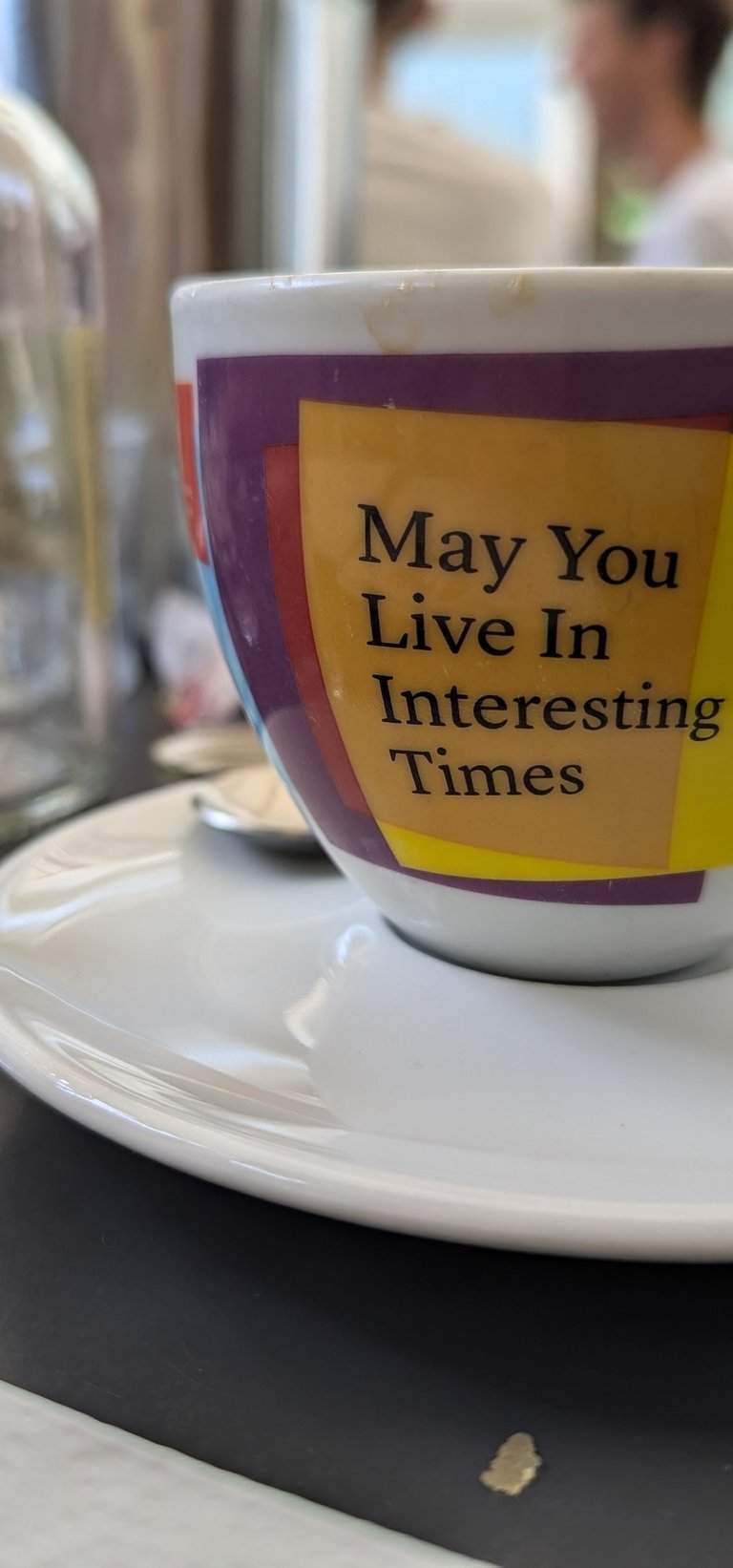 A coffee cup on a table, with the text 'May you live in interesting times' written on the cup.