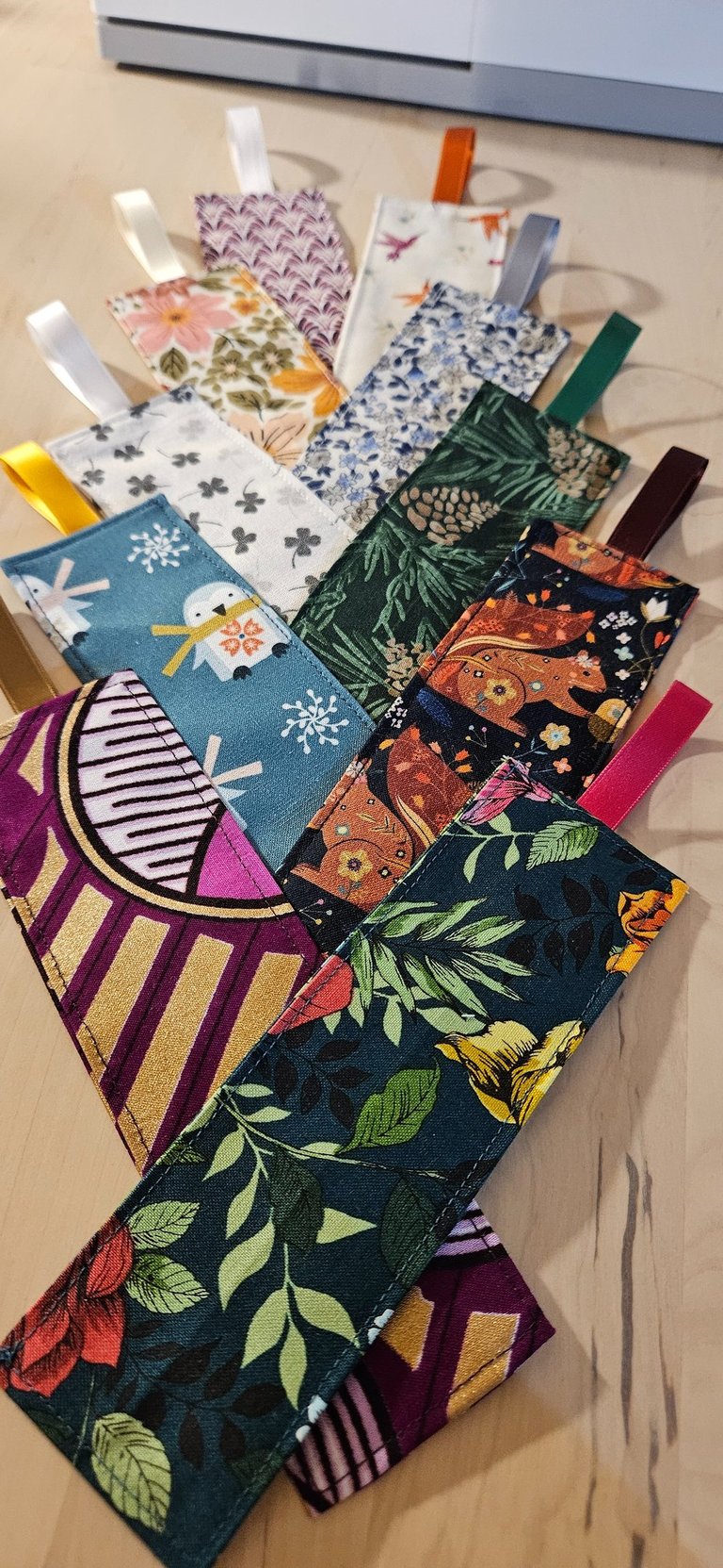 Handmade fabric bookmarks with colorful floral, animal, and geometric patterns and ribbon loops.