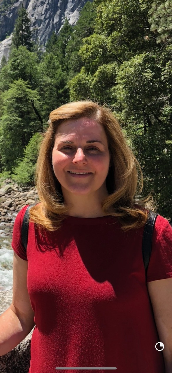 Kathy Fowler, owner and baker at Kitty's Confections, smiling outdoors in a red shirt