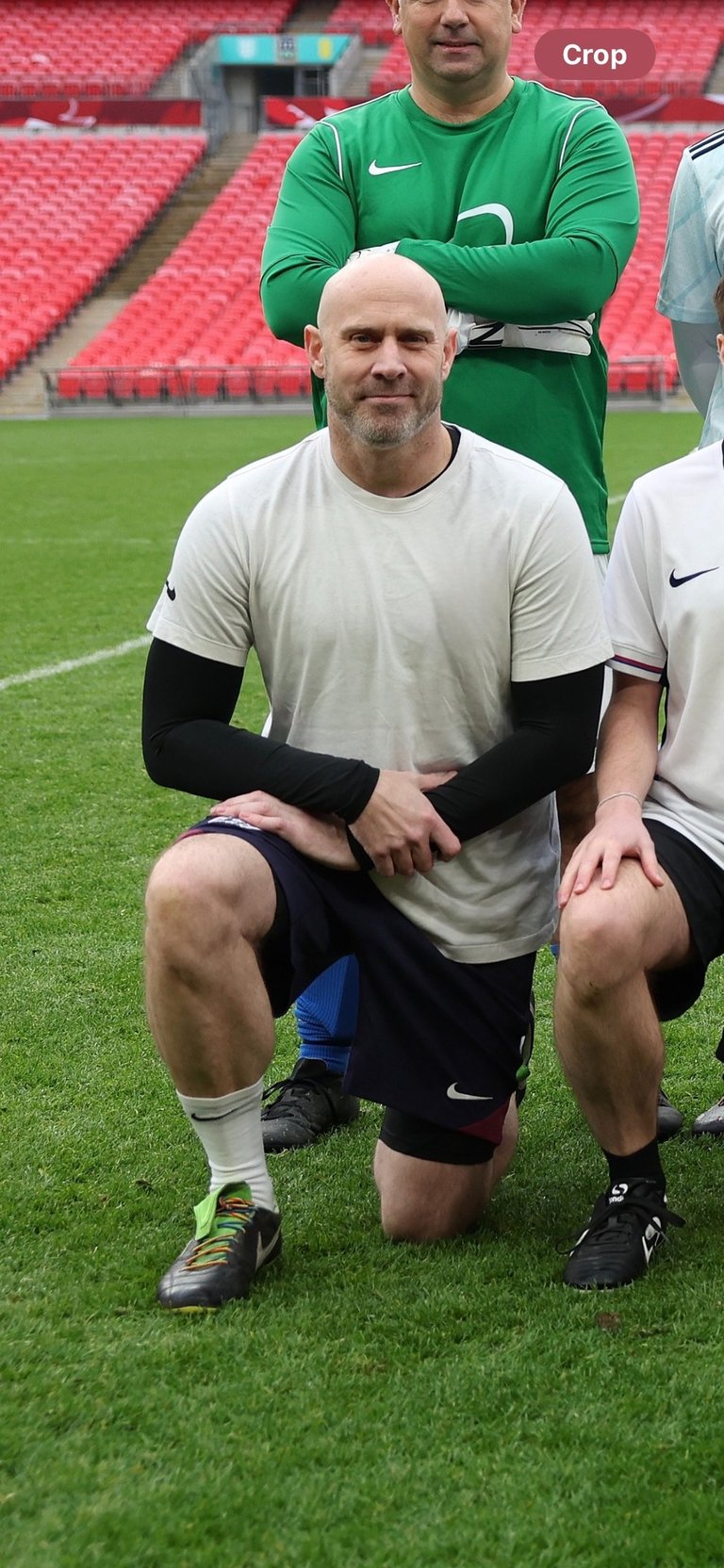 Person kneeling on a football pitch as part of a team photo inside a large stadium with rows of red 