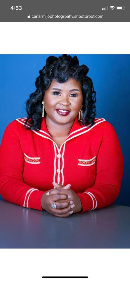 Smiling woman with curled black hair wearing a red sailor-style cardigan with white trim.