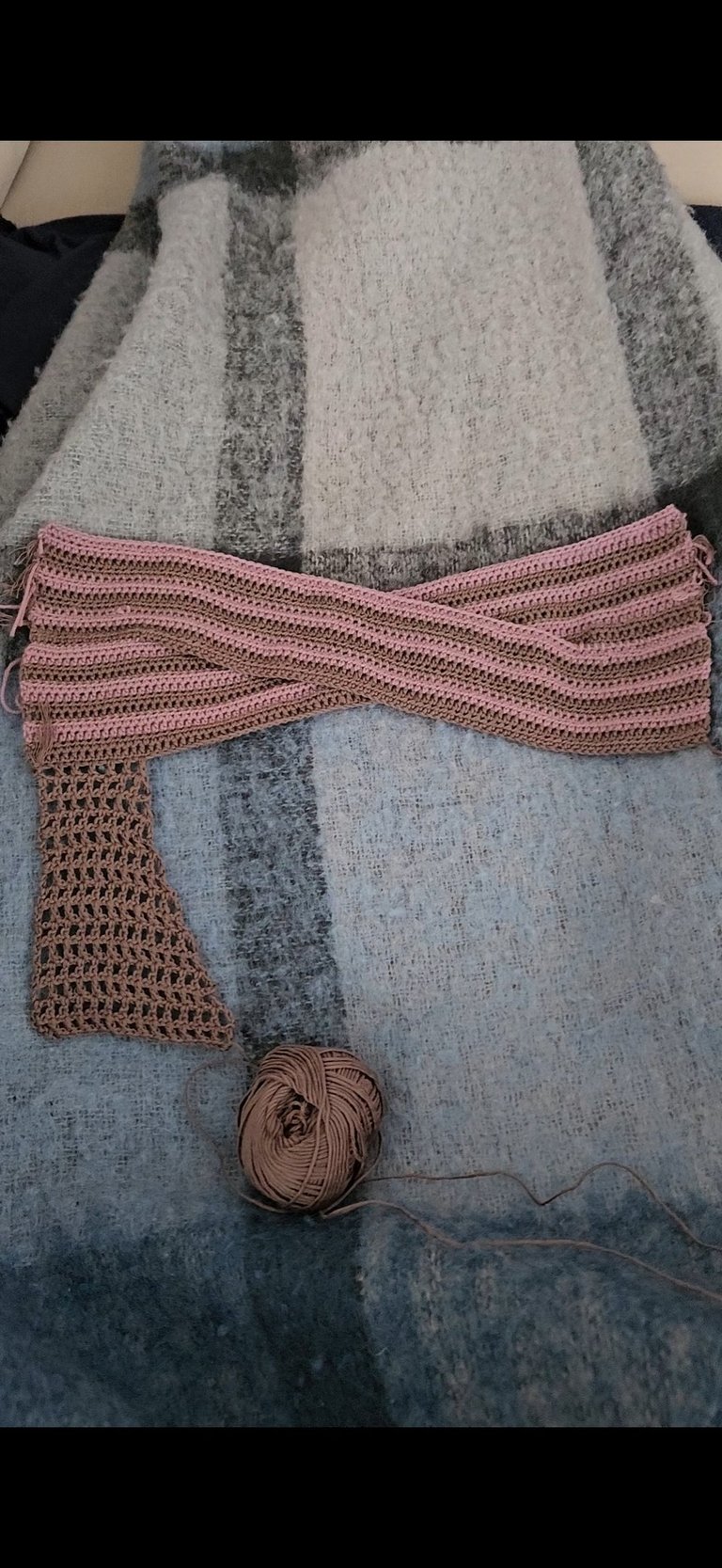 Handmade pink and brown striped crochet scarf project resting on a wool blanket with a ball of yarn.