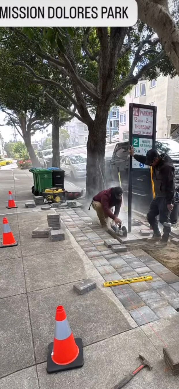 Construction workers installing stone pavers on a sidewalk near Mission Dolores Park in San Francisco.