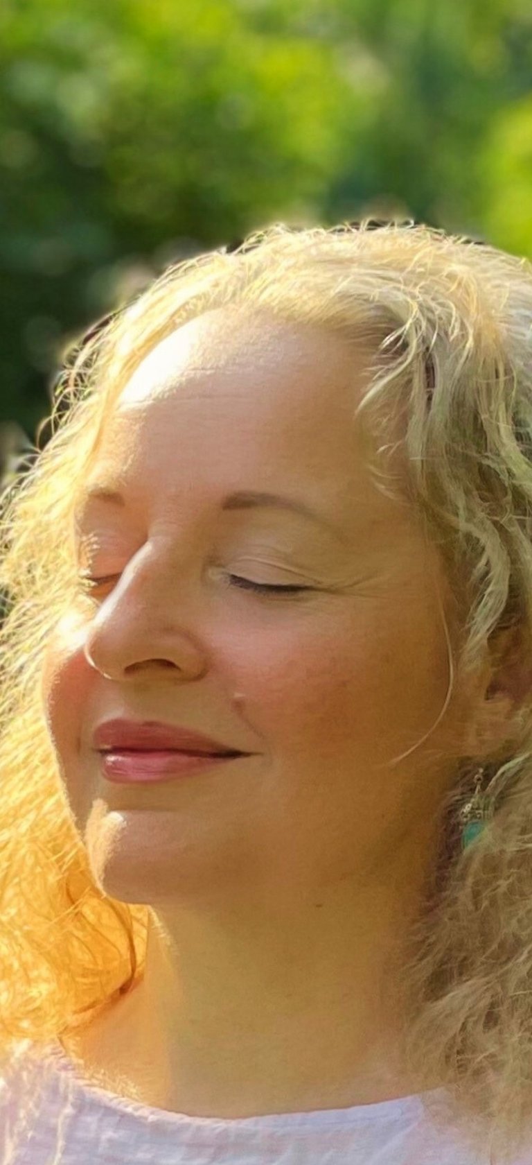 eine lächelnde, blonde Frau mit geschlossenen Augen im Grünen
