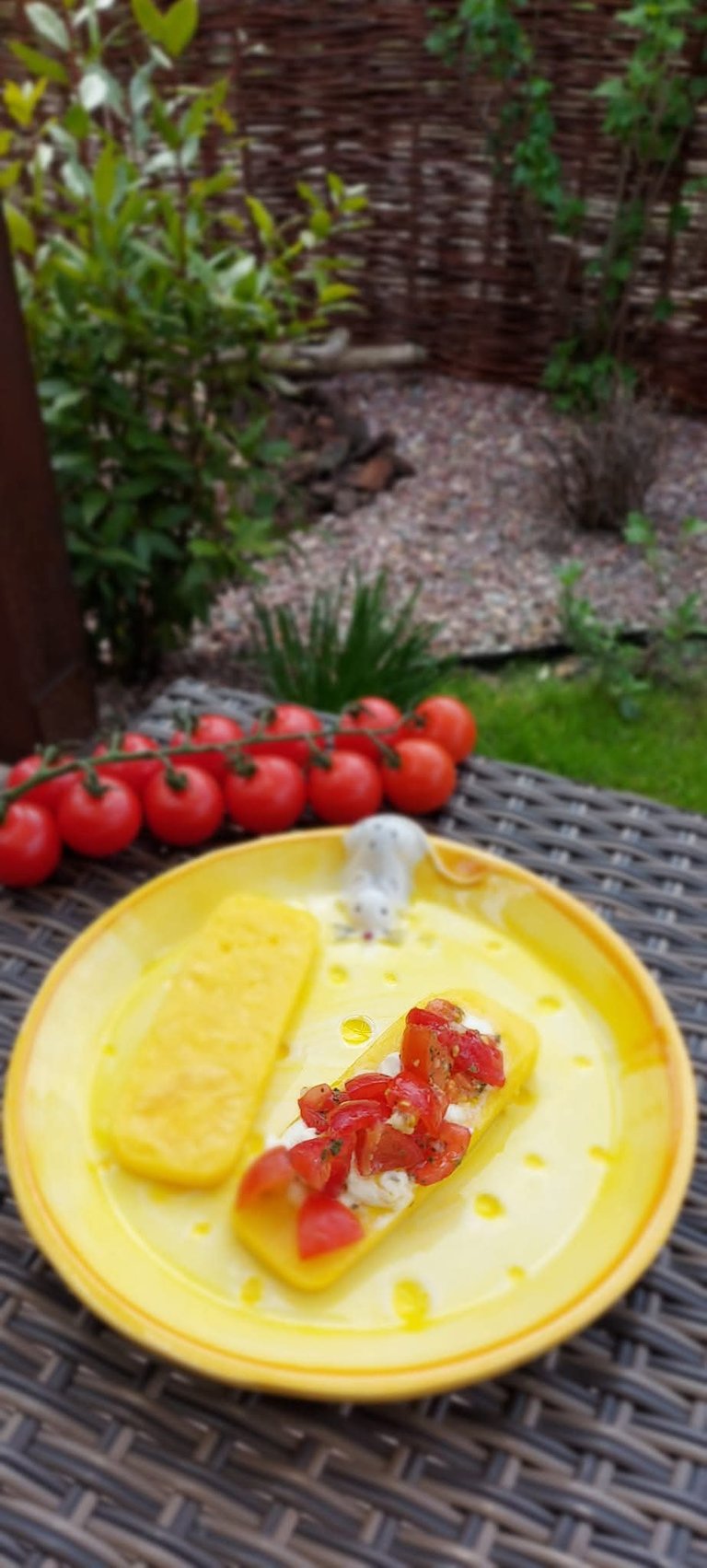 Grilled polenta slices topped with fresh tomato bruschetta on a yellow plate with cherry tomatoes.