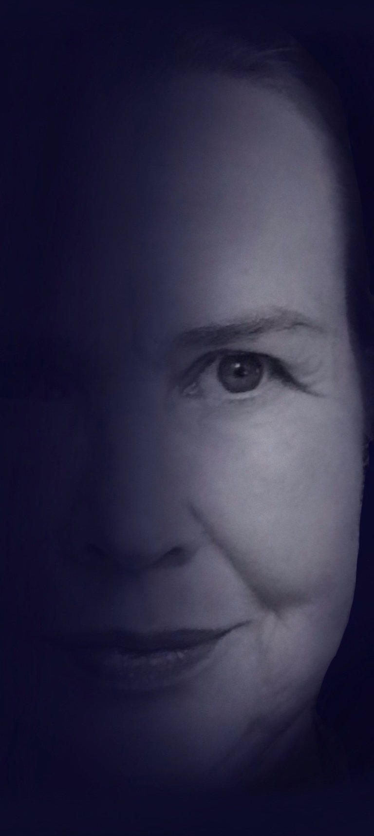 A high-contrast monochrome portrait of a mature woman's face with dramatic lighting and deep shadows.