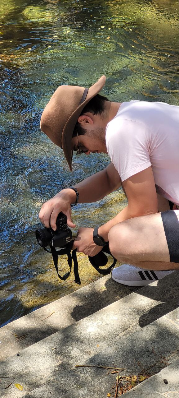a man in a hat taking pitures next to a river