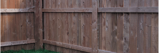 A brown cedar wood privacy fence bordering a lush green backyard lawn with trees in the background.
