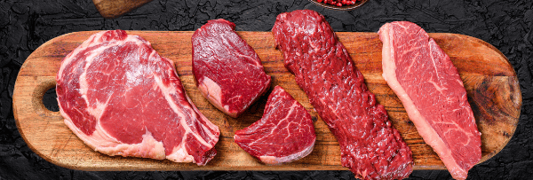 Sélection de morceaux de bœuf cru frais sur une planche en bois.