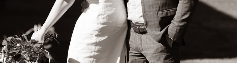 A bride in a white wedding dress and a groom in a suit sharing a kiss outdoors.