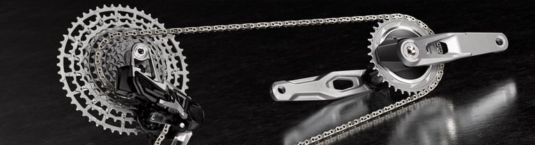 Close-up of a silver bicycle drivetrain featuring a high-performance cassette, chain, and crankset on a dark surface.