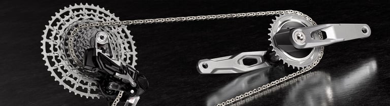 Close-up of a silver bicycle drivetrain featuring a high-performance cassette, chain, and crankset on a dark surface.