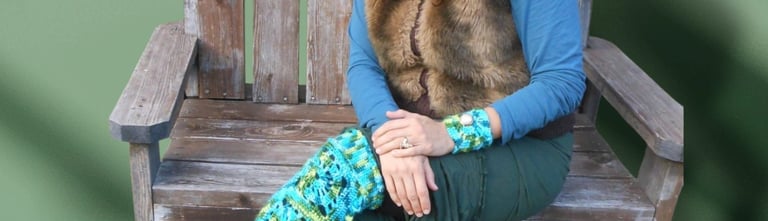 Smiling woman wearing handmade blue and green crochet leg warmers while sitting on a rustic wooden bench.