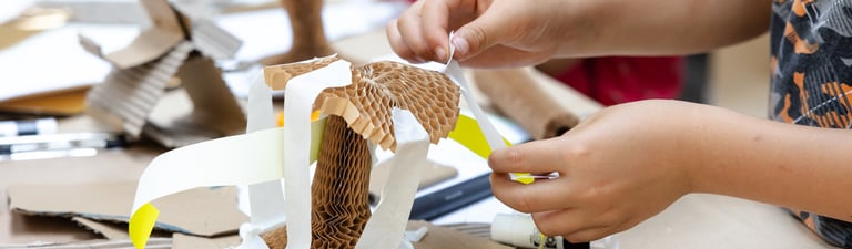 A child sticking paper strips to a concertina cardboard structure.