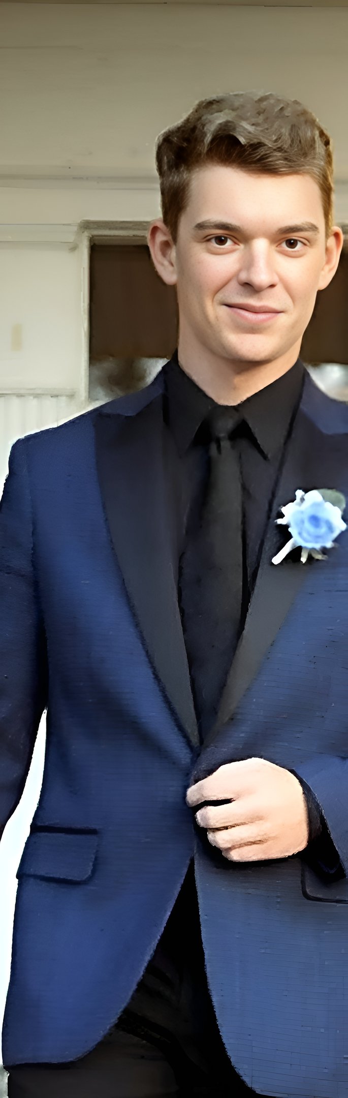 Codie Mills in a navy blue tuxedo with a black lapel, black shirt, and a blue rose boutonniere.