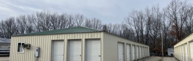 Row of outdoor metal self-storage units with white roll-up doors and gravel driveway. Alberta