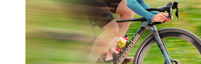 A cyclist riding a Cannondale road bike at high speed on a paved path with motion blur.