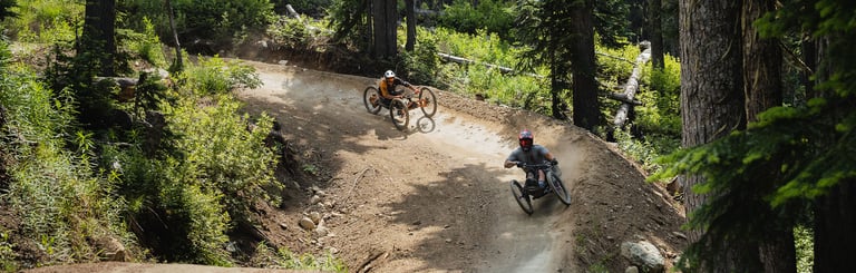 Two adaptive mountain bike riders make their way down the berms of the Whistler Mountain Bike Park.