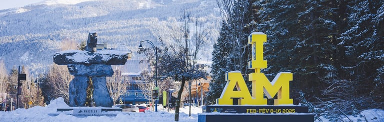 A yellow "I AM" Invictus Games sign in front of a snow-covered Whistler village