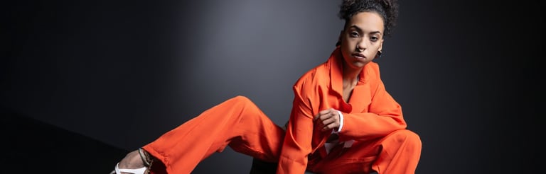 Moderne Portraitfotografie einer Frau in leuchtendem orangem Anzug vor grauem Hintergrund in Chur