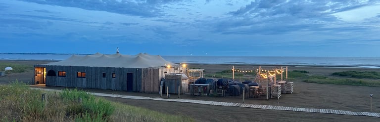 Bar de plage rustique et patio extérieur avec guirlandes lumineuses sur une plage de sable