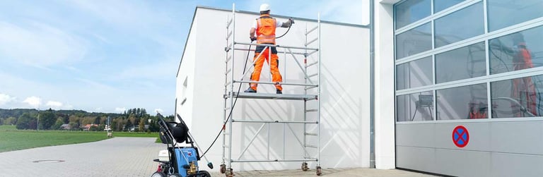 Un ouvrier sur un échafaudage utilise un nettoyeur haute pression pour nettoyer un bardage