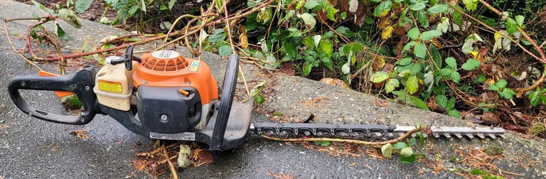 a picture of a hand held gas power hedge trimmer sitting on the ground