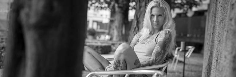 Outdoorshooting einer blonden Frau mit Tattoos sitzt entspannt auf Bank in schwarz-weiss Portrait von Fotograf in Chur