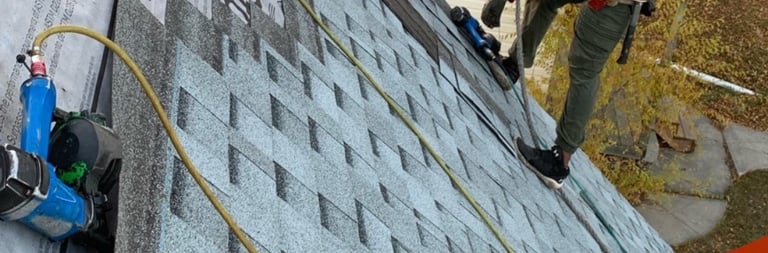 Professional roofing contractor installing new asphalt shingles on a steep residential roof with safety harness.