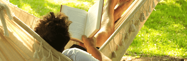 Vīrietis vasarā šūpuļtīklā lasa grāmatu