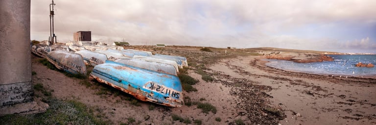 Weathered fishing boats on a coastal beach with peeling paint and textured surfaces under soft evening light
