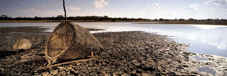 Fine art panorama of traditional woven fishing baskets on cracked riverbank soil beside still water in Zimbabwe.