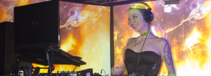 A smiling woman DJing in front of huge visual screens