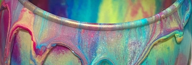 A glass used for a multi color acrylic paint pour shows a vibrant rainbow dripping from the rim