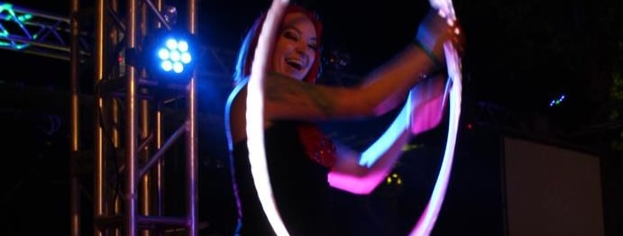 A performer with red hair spins a glowing LED hula hoop during a night stage show. 