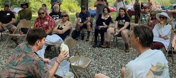A group of people attending an outdoor educational workshop sitting in a circle on gravel.