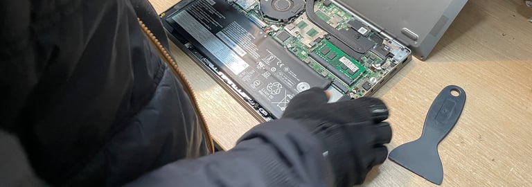 A technician repairing an open laptop computer on a wooden workspace.