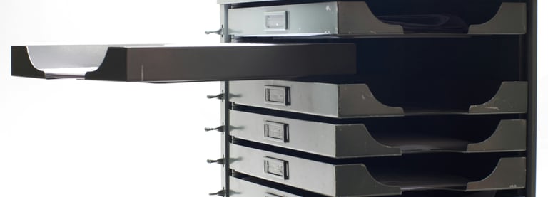 A black and white image of a set of documents drawers with one open drawer