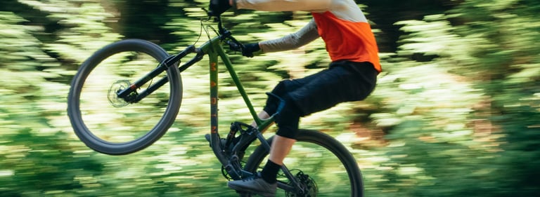 Mountain biker performing a manual wheelie on a green Marin bike through a sunlit forest trail.