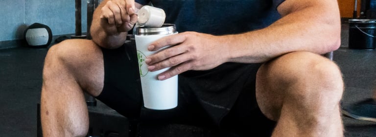 A man scoops whey protein powder into a white shaker bottle for a post-workout recovery drink.