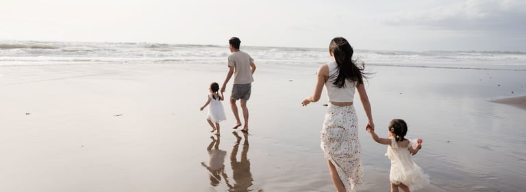 Family walking across shallow water reflections at Petitenget Beach Seminyak Bali during a beach family photography session