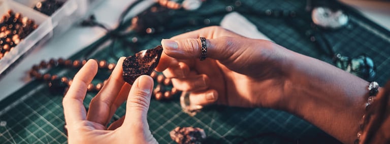 Manos de una joyera sosteniendo una piedra preciosa oscura sobre una base de corte verde