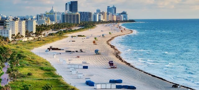 Vista aérea de uma longa praia com prédios ao fundo e mar azul em Miami